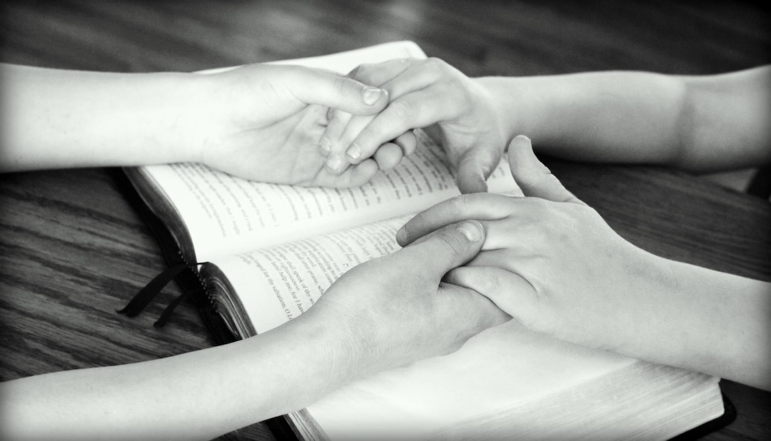 Två personer som håller varandra i händerna med en bibel under